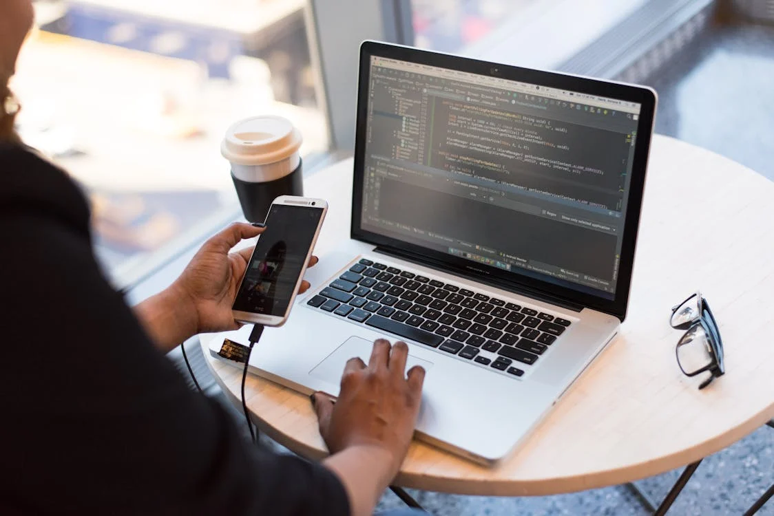 App development codes mobile app development of a person holding a smartphone while using laptop