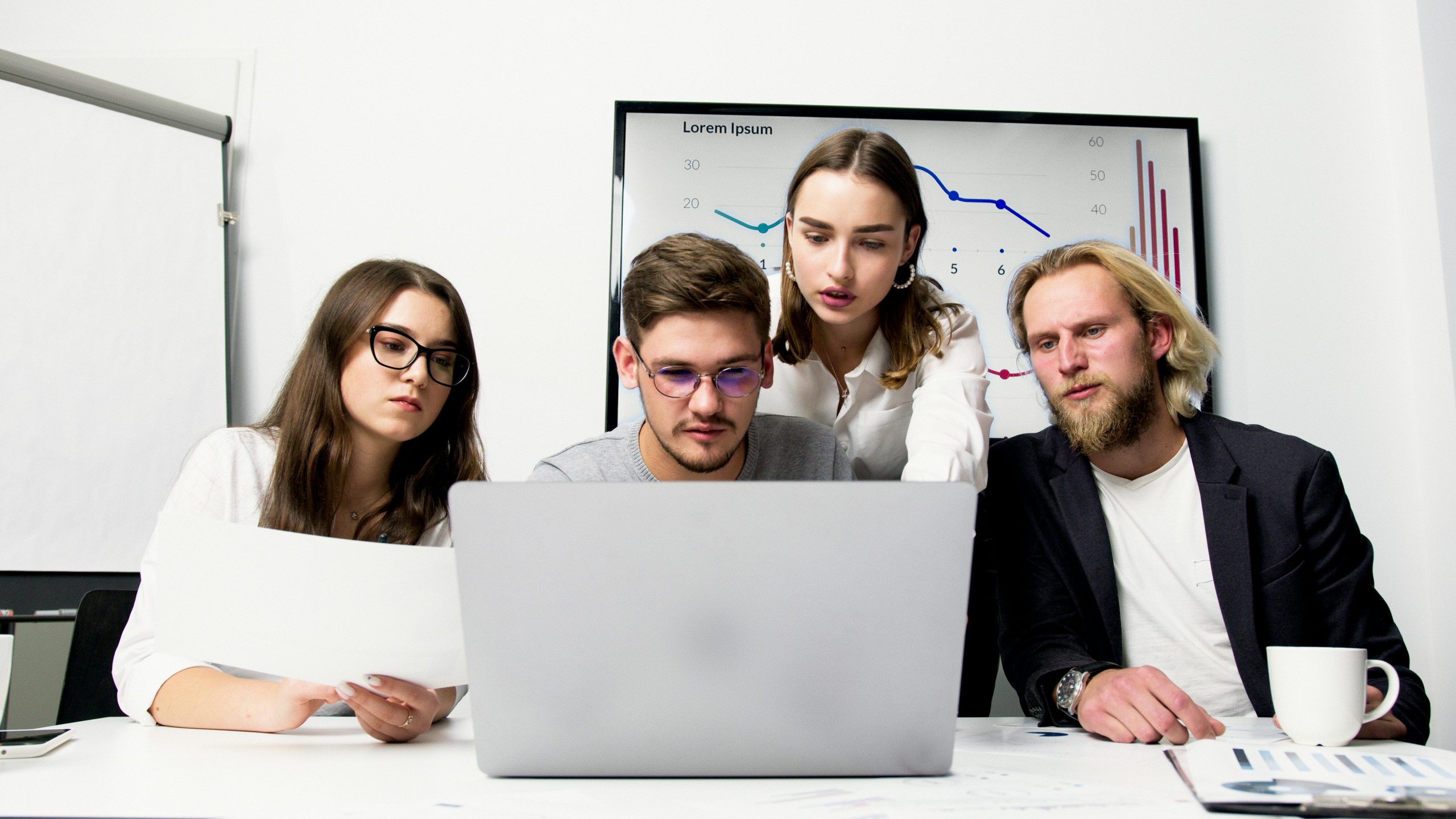 A team of four members gathered for a meeting on mastering online branding for a startup business, all focused on a laptop screen.