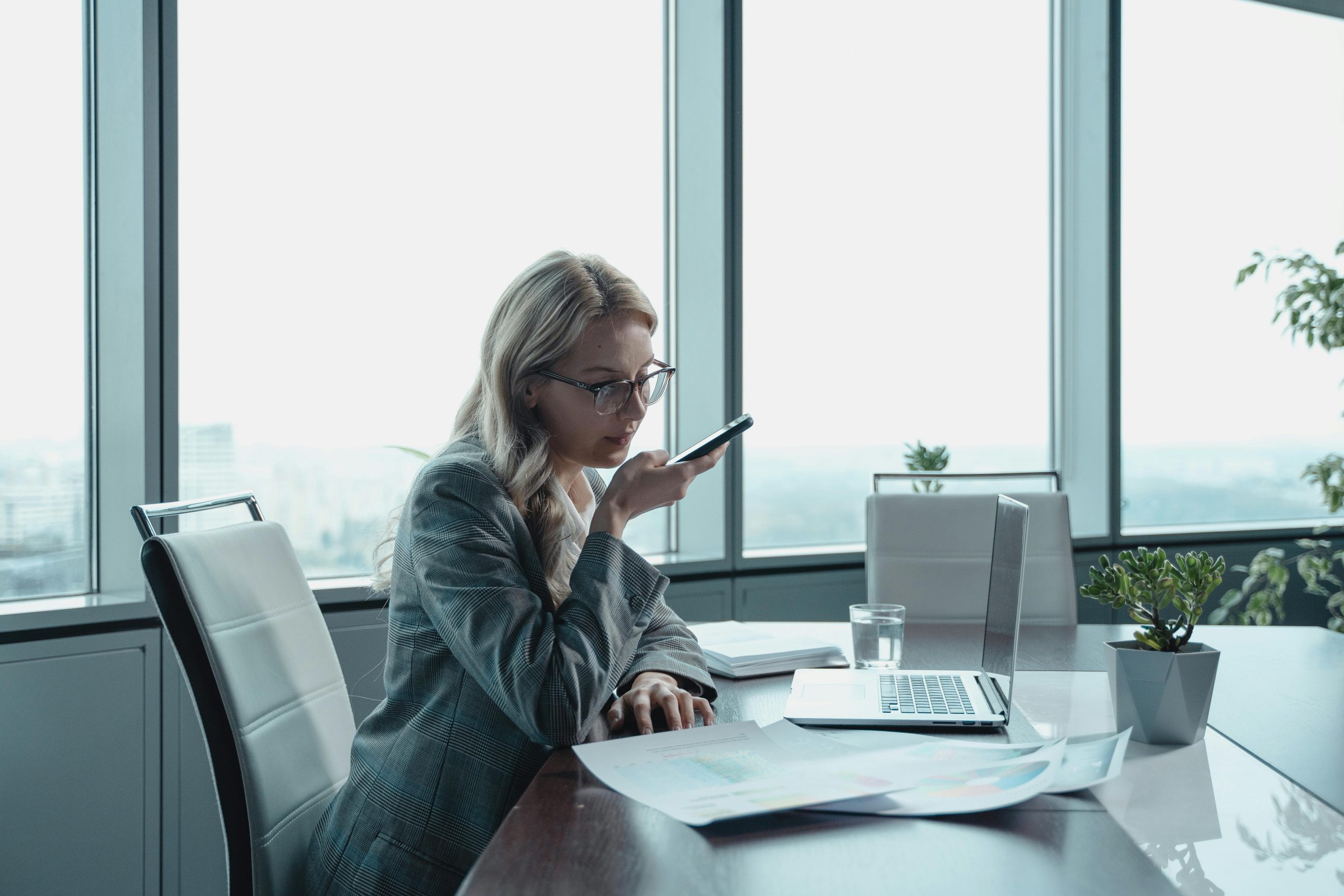 Woman in a gray jacket sitting on a chair using a MacBook and activating voice search.